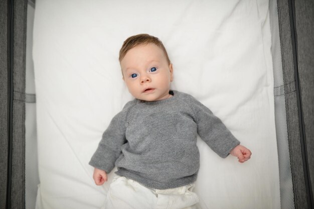 Baby mit blauen Augen mit grauem Pullover morgens in seinem Bett