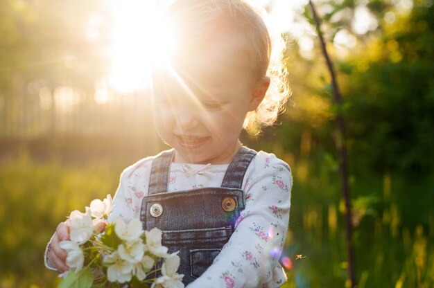 Baby mit Blumenstrauß von Blumen im Garten im Sonnenlicht. Apfelblüte.