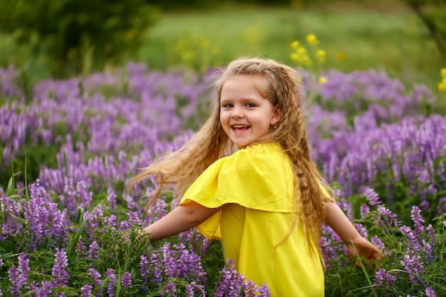 Baby mit den Locken, die auf einem Gebiet des Lavendels, gekleidet in einem gelben Sommerkleid, Sommerabend spinnen