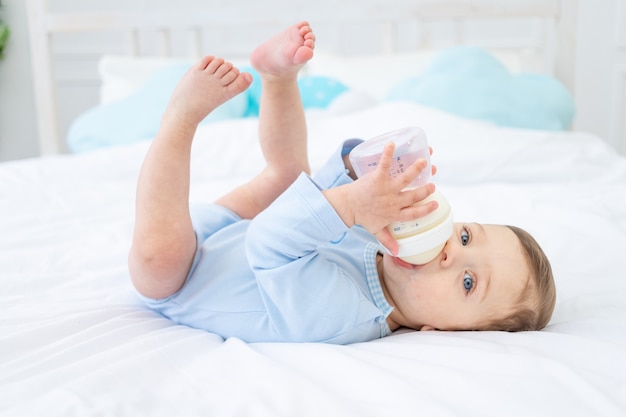 Baby mit einer Flasche Milch auf dem Bett zum Schlafen in einem blauen Bodysuit, Babynahrungskonzept