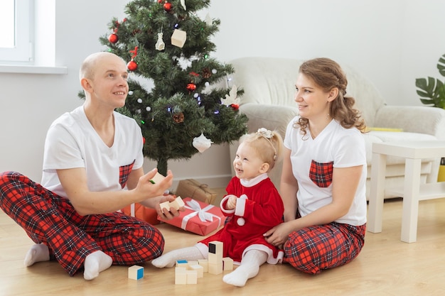 Baby mit Hörgerät und Cochlea-Implantat, das sich mit den Eltern im Weihnachtszimmer amüsiert Gehörlose Vielfalt und Gesundheit und Vielfalt