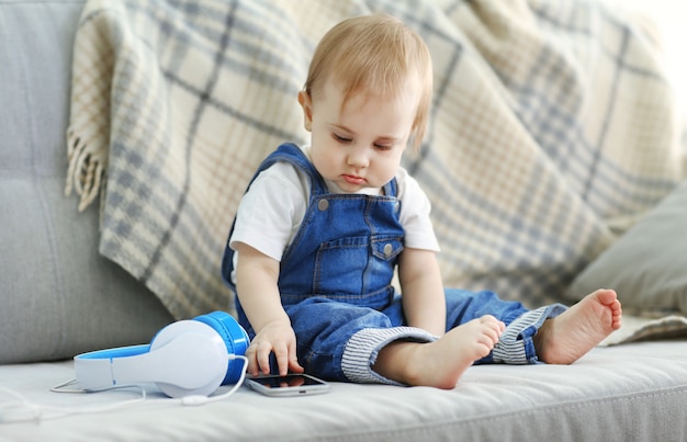 Baby mit Kopfhörern, die auf Sofa sitzen