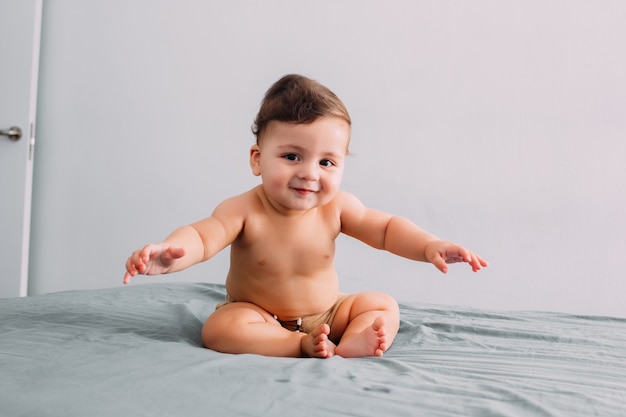 Baby mit lustigem Gesicht sitzt auf dem Bett, Gesichtsausdruck