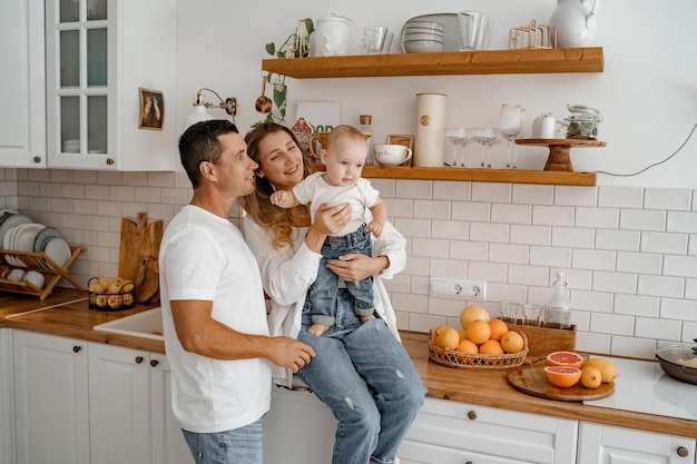 Baby mit Mama und Papa in der Küche, gekleidet in Jeans und weißen T-Shirts