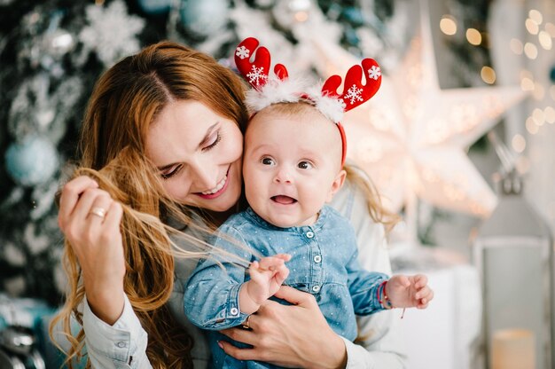 Baby mit Mutter auf Boden nahe Weihnachtsbaum. Fröhliche Weihnachten. Weihnachten dekoriertes Interieur. Das Konzept des Familienurlaubs.