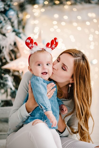 Baby mit Mutter auf Boden nahe Weihnachtsbaum. Frohes neues Jahr und frohe Weihnachten.