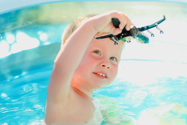 Baby mit Spielzeugflugzeug im Swimmingpool. Kleiner Junge, der lernt, im Außenpool zu schwimmen.