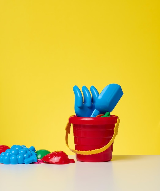 Baby roter Plastikeimer mit Schaufel und Spielzeug auf gelbem Grund. Outdoor-Artikel