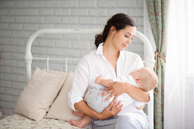 Baby schläft auf der Brust der Mutter. Junge schöne Mutter, die sich nach der Geburt erholt. Junge Mutter, die Baby mit Zärtlichkeit kuschelt.