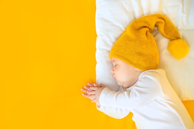 Baby schläft mit Hut auf gelbem Hintergrund, Winter- und Feiertagskonzept