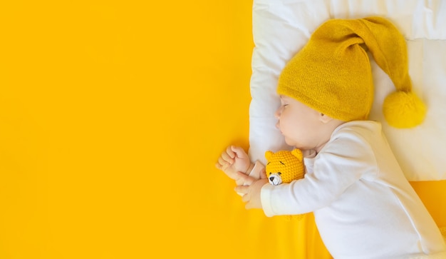 Baby schläft mit Hut auf gelbem Hintergrund, Winter- und Feiertagskonzept