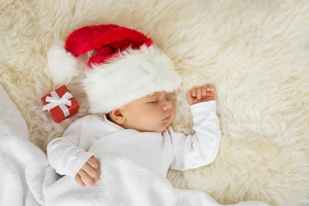Baby schläft mit Weihnachtsmütze und Geschenkbox