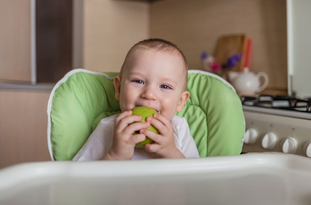 Baby sitzt auf einem Stuhl und isst grünen Apfel. Baby isst die richtige Ernährung. Ökologische Produkte