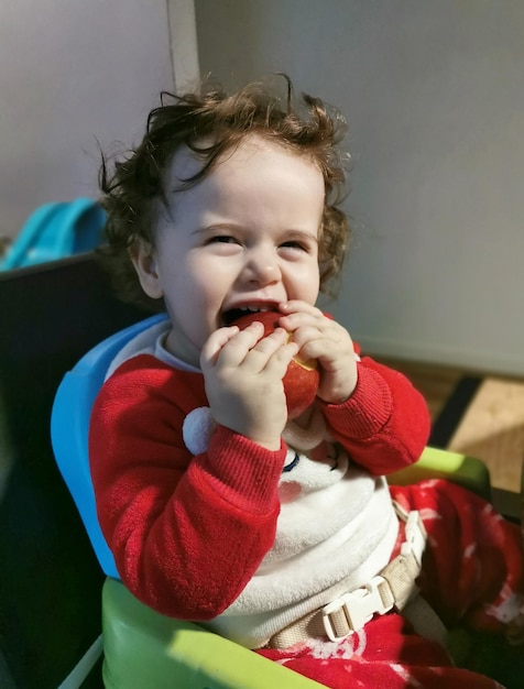 Baby sitzt im Kinderstuhl und isst allein einen Apfel