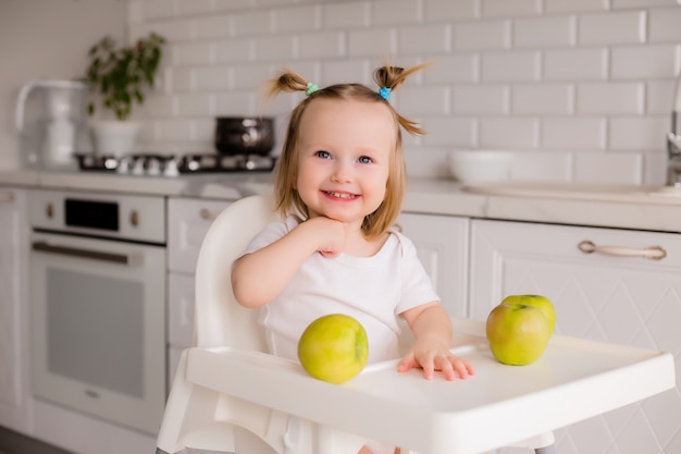 Baby sitzt in einem Kinderstuhl in der Küche und isst grüne Äpfel