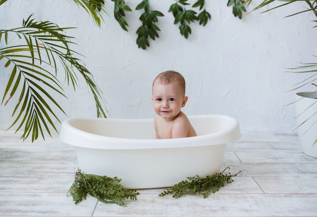 Baby sitzt in einem weißen Bad auf einer weißen Oberfläche mit Pflanzen