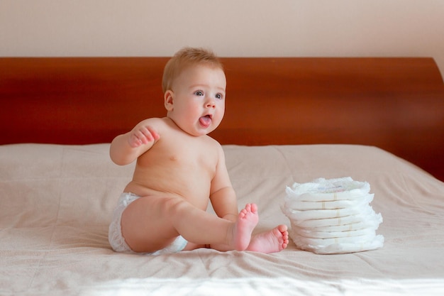 Baby sitzt in einer Windel auf dem Bett im Schlafzimmer