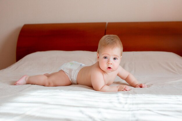 Baby sitzt in einer Windel auf dem Bett im Schlafzimmer