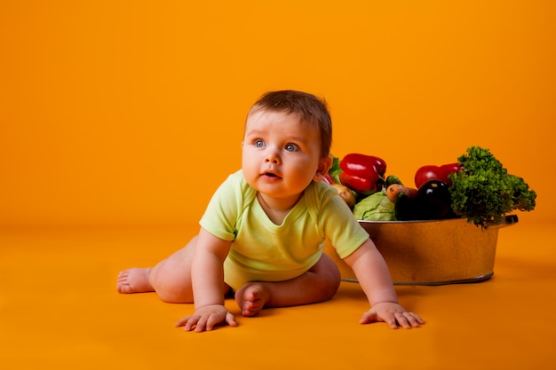 Baby sitzt neben dem Becken mit frischem Gemüse. Konzept umweltfreundlicher landwirtschaftlicher Produkte