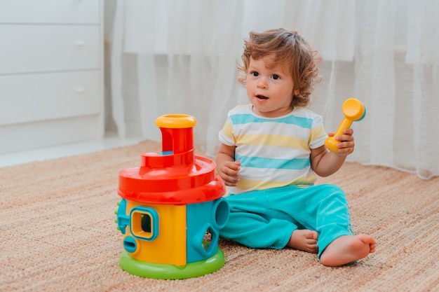 Baby spielt auf dem Boden im Raum mit lehrreichem Plastikspielzeug