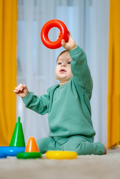 Baby spielt mit Pyramidenspielzeug. Niedlicher kleiner Junge spielt mit Spielzeug, während er auf dem Boden sitzt. Entwicklung der Feinmotorik