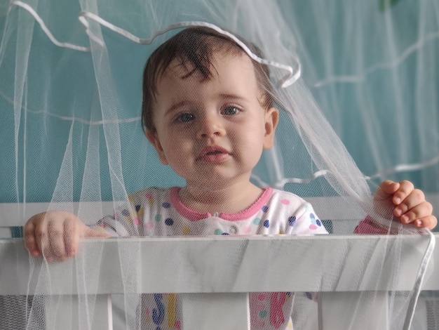 Baby steht im Kinderbett, geschützt durch das Moskitonetz.