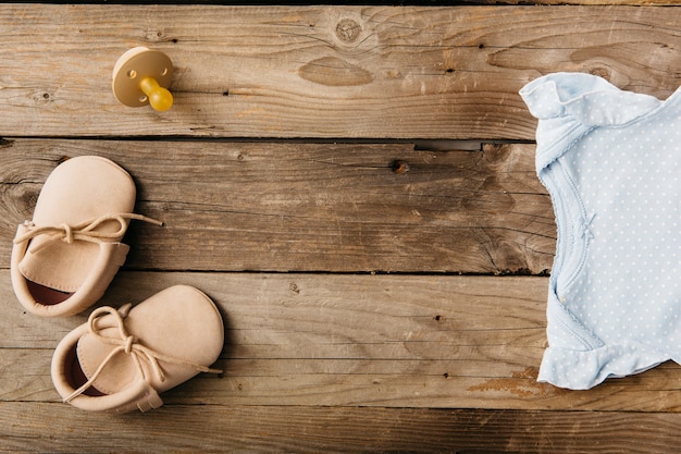 Foto baby-strampelanzug; paar schuhe und schnuller auf holztisch