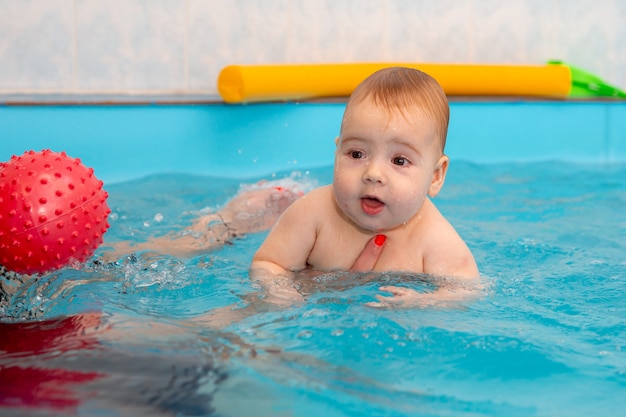 Baby trainiert, um im Pool mit einem Trainer zu schwimmen