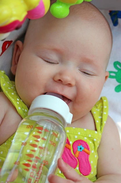 Baby trinkt aus der Flasche, während es im Kinderwagen liegt. Füttern des Babys. Kleines Mädchen lächelt und trinkt aus der Flasche. Neugeborenes isst