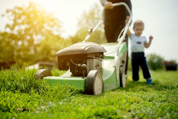 Baby und sein Großvater mähen das Gras mit Rasenmäher.