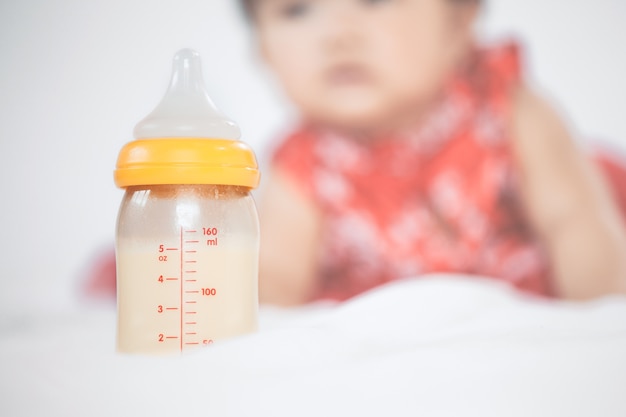 Babyflasche mit der Muttermilch für das Stillen auf kleinem Babymädchenhintergrund.