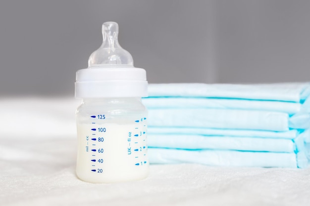 Babyflasche mit Milch und Windeln auf weißem Stoffhintergrund Babypflege Erste Lebenstage Fütterung und Mutterschaft