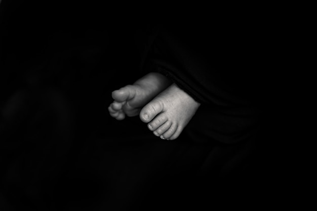 Babyfüße auf schwarzem Hintergrund Neugeborenen-Fotografie-Idee. Negatives Weltraumfoto