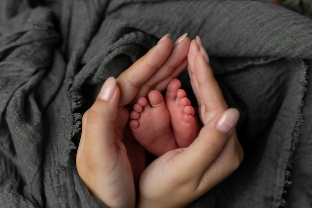 Babyfüße in den Händen der Mutter. Beine eines winzigen Neugeborenen in den Armen, Nahaufnahme. Familie und Kind. Fröhliche Fa