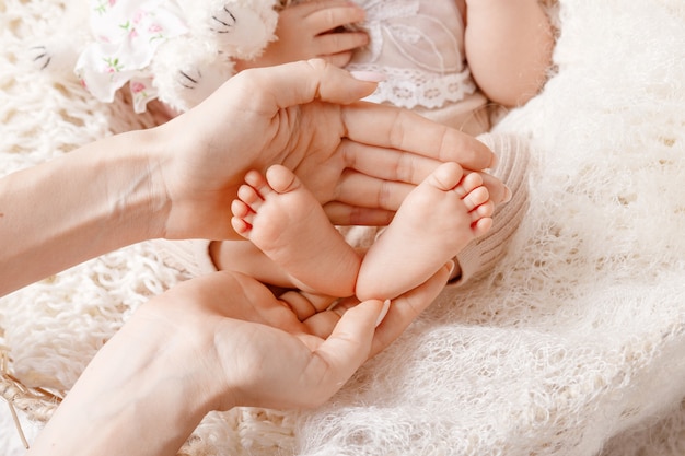 Babyfüße in Mutterhänden. Winzige neugeborene Babyfüße auf weiblicher geformter Handnahaufnahme
