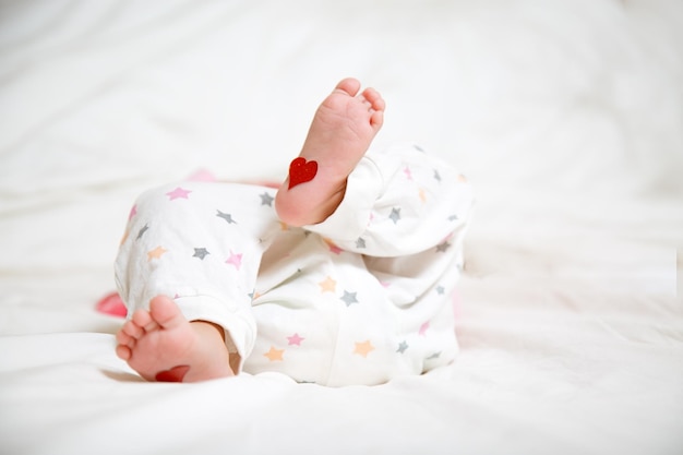 Babyfüße mit Herzen an den Füßen Ein neugeborenes Baby liegt auf dem Bett