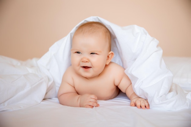 Babyjunge in einer windel liegt auf einem weißen laken, bedeckt mit einer decke im schlafzimmer auf dem bett