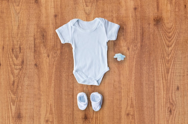 Babykleidung, Babyalter, Mutterschaft und Objektkonzept - Nahaufnahme von weißem Bodysuit, Stiefeletten und Schnuller für neugeborene Jungen auf Holztisch