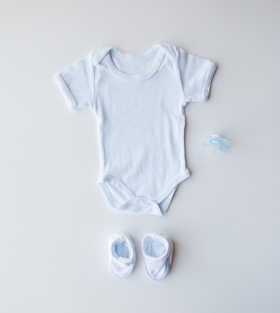 babykleidung, babyhood, mutterschaft und objektkonzept - nahaufnahme von weißem bodysuit, stiefeletten und schnuller für neugeborenen jungen auf dem tisch