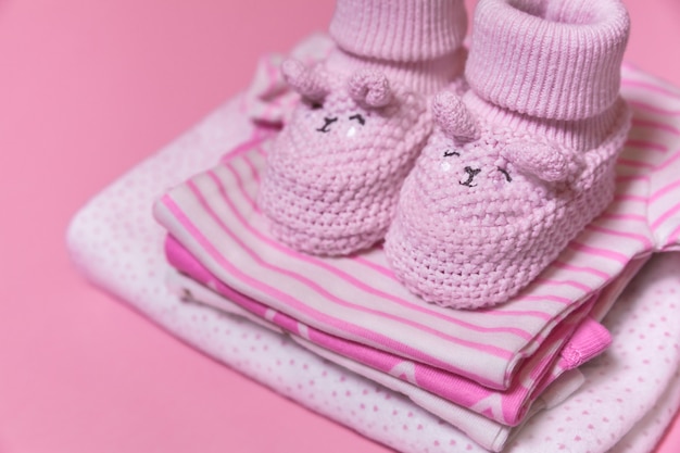 Babykleidung und Häkelschuhe für neugeborenes Mädchen auf einem rosa Hintergrund