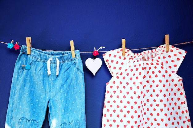 Babykleidung und -waren, die an Wäscheklammern auf der Wäscheleine auf einem strukturierten Wandhintergrund hängen