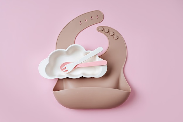 Babylätzchen und Teller in Form einer Wolke auf rosa Hintergrund. Baby dienen. Konzept von Kindermenü, Ernährung und Fütterung