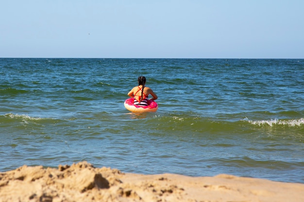 Babymädchen auf dem Meer mit einem rosa Rettungsring an einem Sommertag, Urlaub