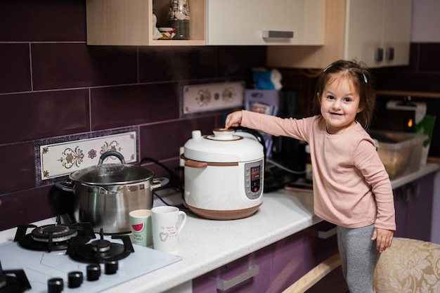 Babymädchen bereiten das Abendessen zu Hause in der Küche mit Slow Cooker zu und setzen Dampf aus dem Dampfgarer frei