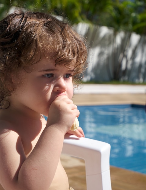 Babymädchen, das an einem sonnigen Tag eine Banane am Pool isst.