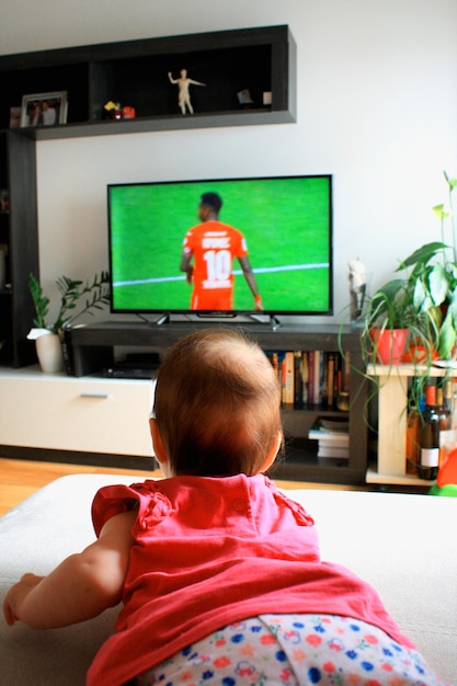 Babymädchen, das einen Fußball im Fernsehen anschaut