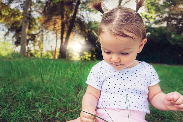 Babymädchen, das im Gras im Park sitzt und die Natur berührt, spielt und erkundet Süßes Kind, das draußen den Sommer genießt