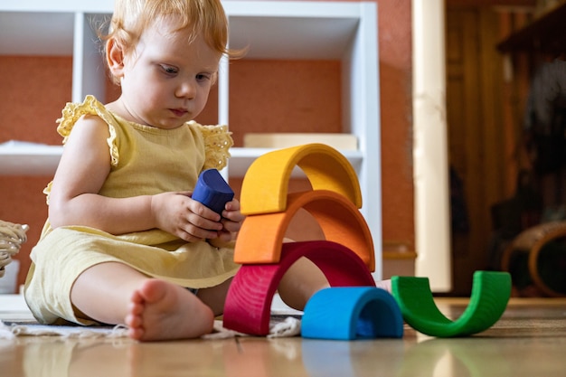 Babymädchen im Kleid, das Regenbogenbogenblockbau baut, der ökologischen hölzernen Spielzeugturm baut