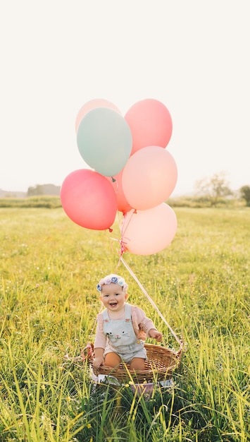 Babymädchen im Weidenkorb mit rosa Luftballons im Sonnenlicht im Sommer Glückliches Kind in der Natur Erste Geburtstagsfeier Familie feiert einjähriges Baby im Freien Foto von Kindheitsträumen Urlaub