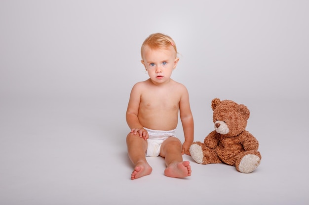 Babymädchen in der Windel, die mit Teddybären auf weißem Hintergrund spielt